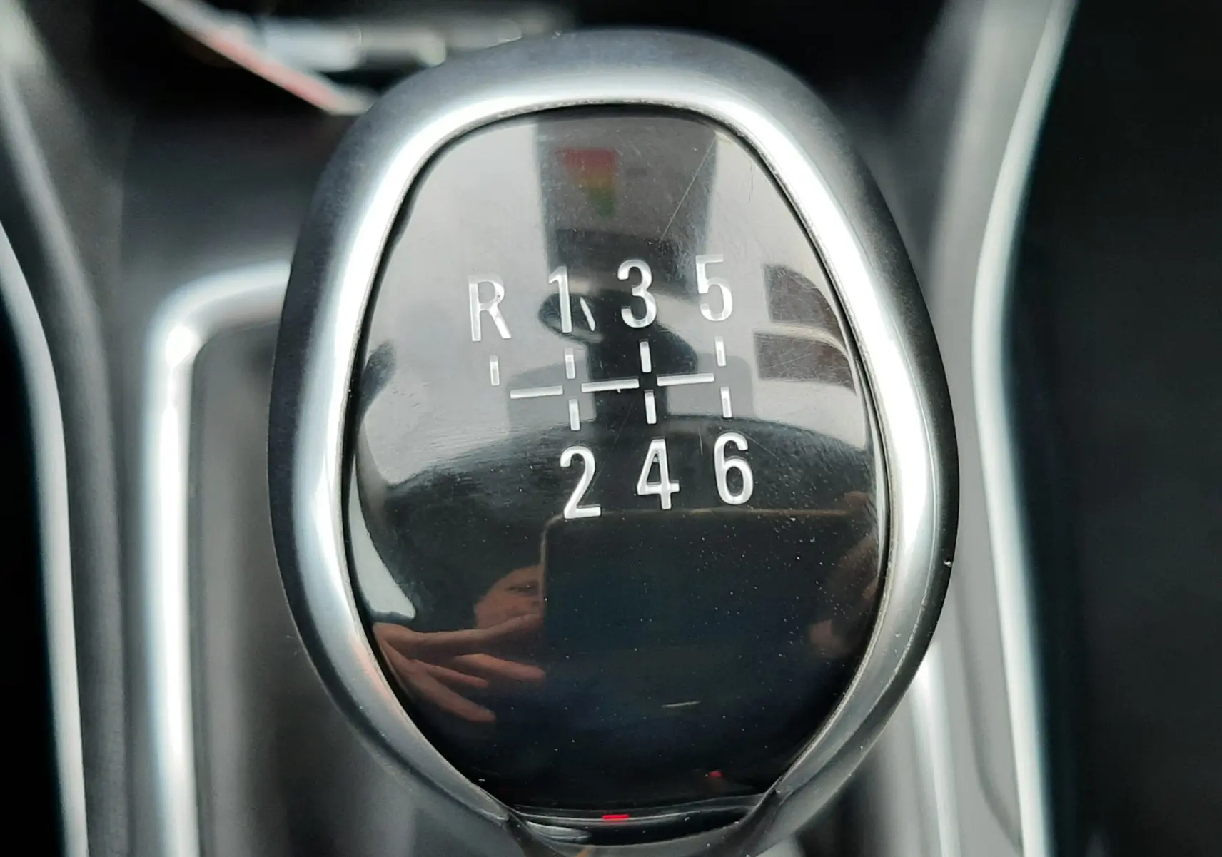 Gros plan sur le levier de vitesses manuel noir brillant de la Peugeot 308 SW gris Artense, montrant les six rapports et la marche arrière.