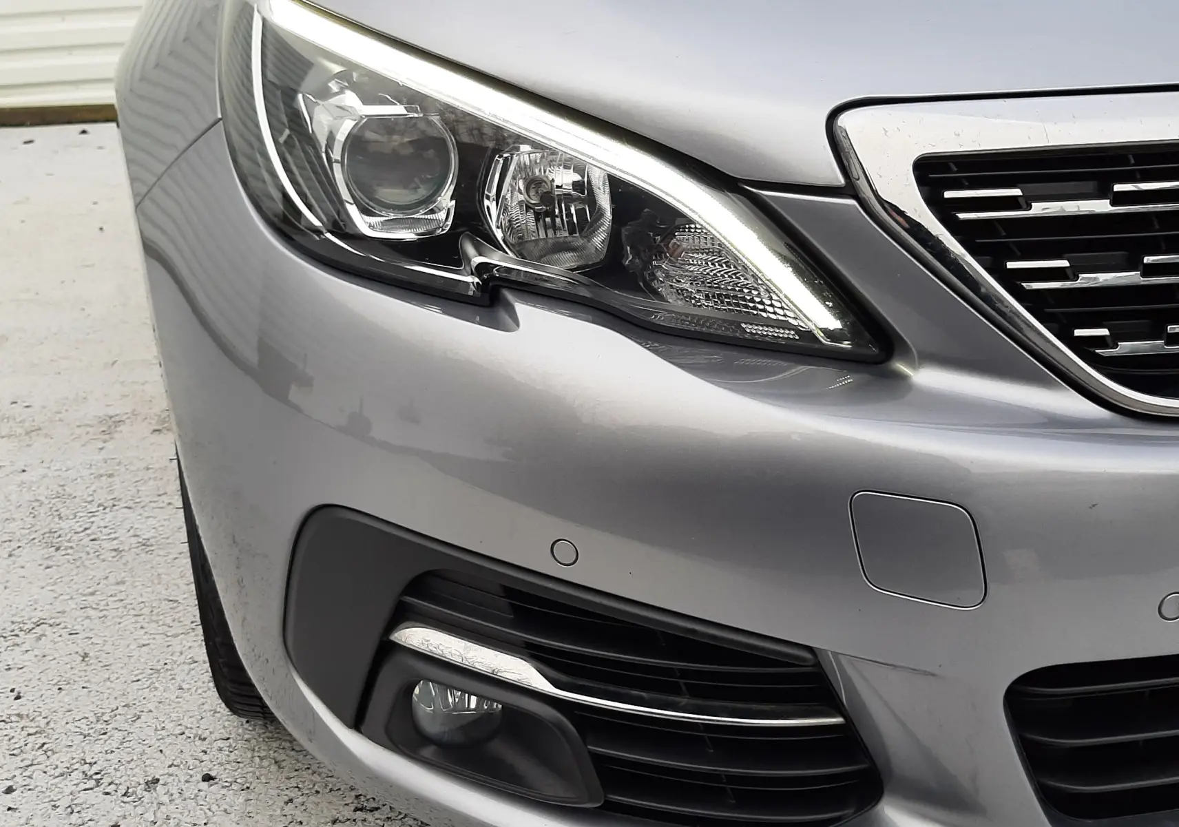Gros plan sur l'avant droit gris Artense de la Peugeot 308 SW 2021, mettant en valeur le phare LED et la calandre.