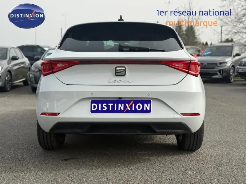 Vue arrière d'une SEAT Leon blanche Nevada métallisée, avec feux arrière LED et logo central sur un parking.