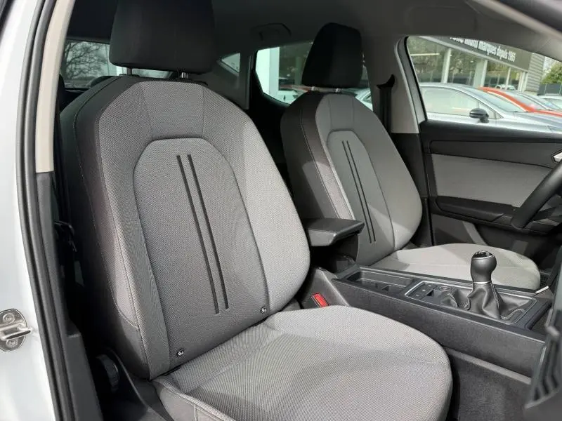 Vue intérieure sur les sièges avant gris/noir du SEAT LEON 2025, avec accoudoir central et levier de vitesse manuel.