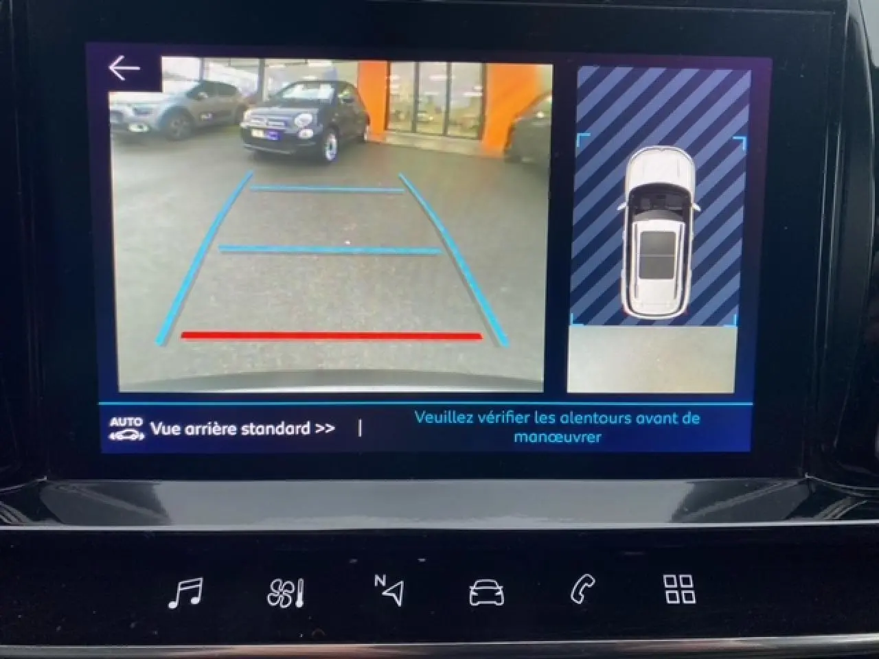 Écran de caméra de recul montrant une voiture grise en 3/4 arrière avec lignes de guidage bleues et rouges.