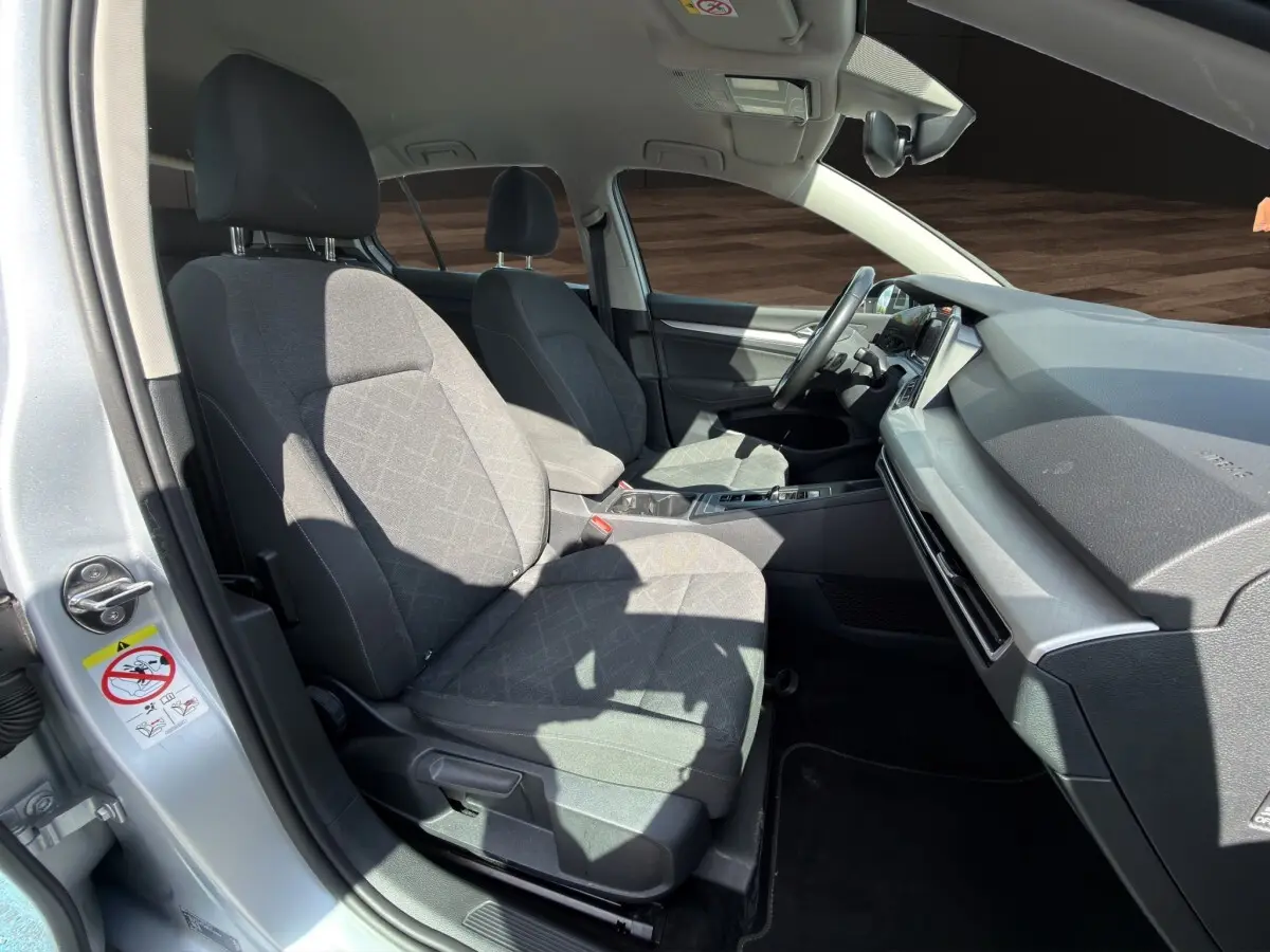 Vue intérieure côté conducteur d'une Volkswagen Golf gris clair 2022, sièges tissu gris et tableau de bord moderne.
