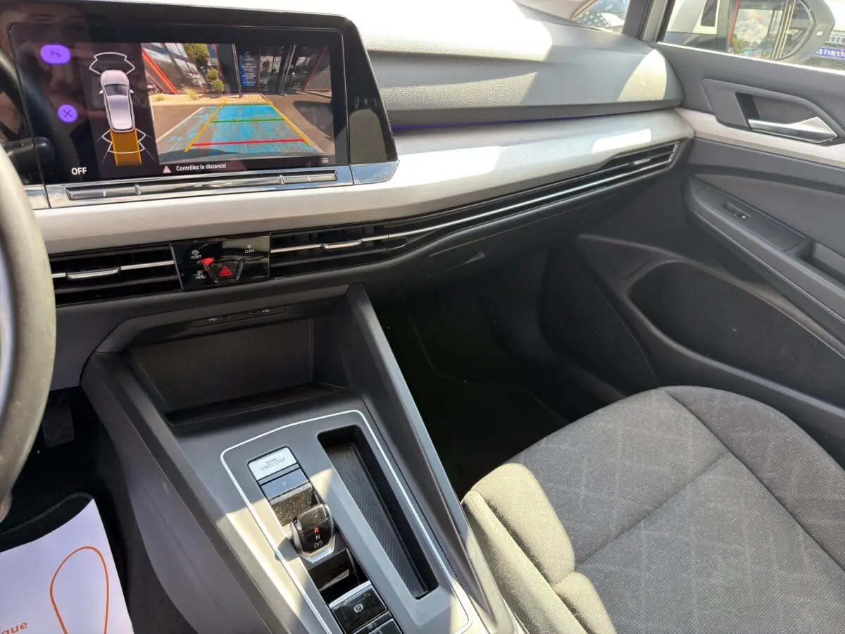 Vue intérieure côté passager de la Volkswagen Golf grise avec écran de recul et console centrale moderne.