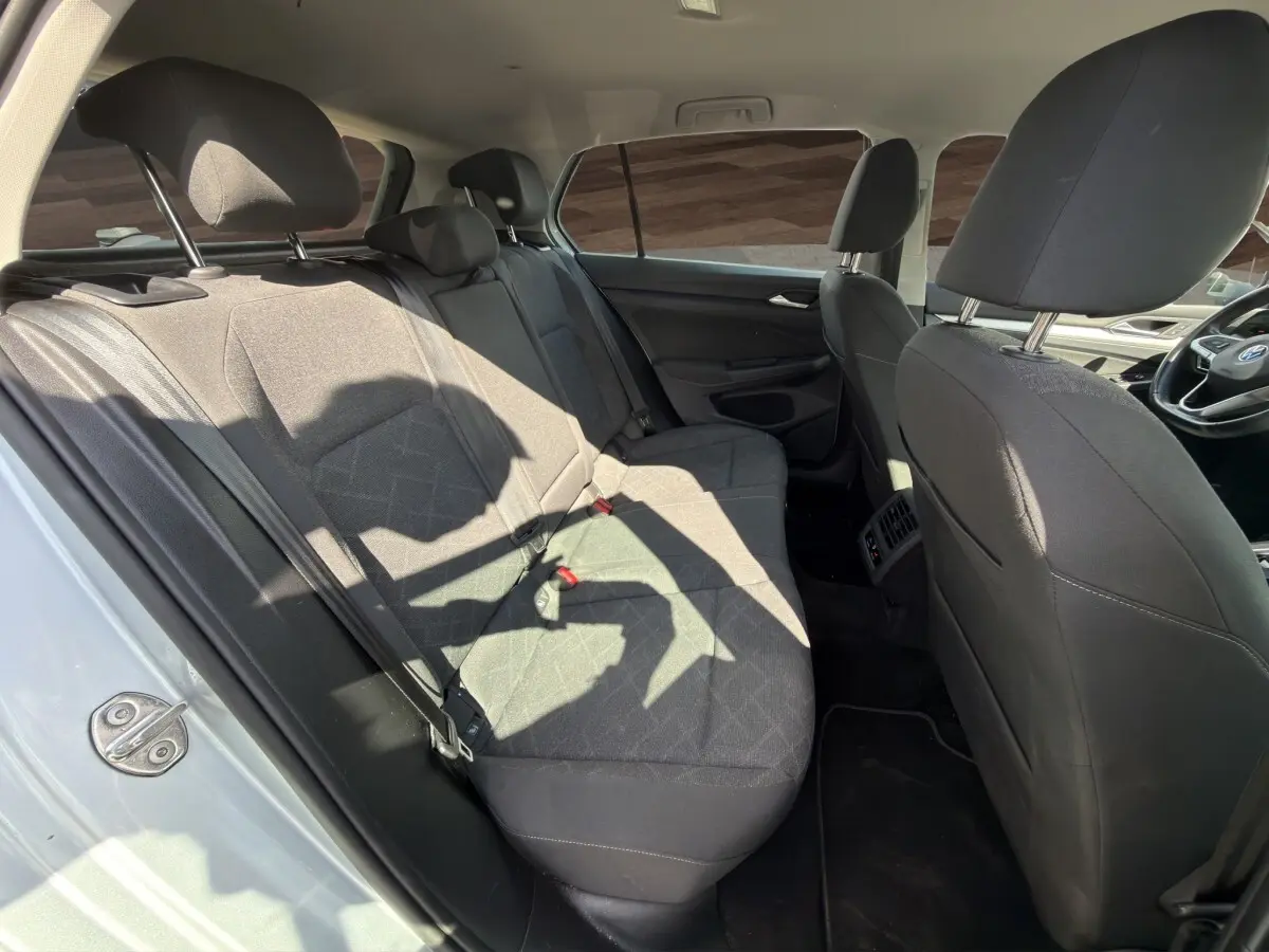 Vue intérieure côté gauche montrant la banquette arrière noire et les sièges avant d'une Volkswagen Golf gris clair 2022.