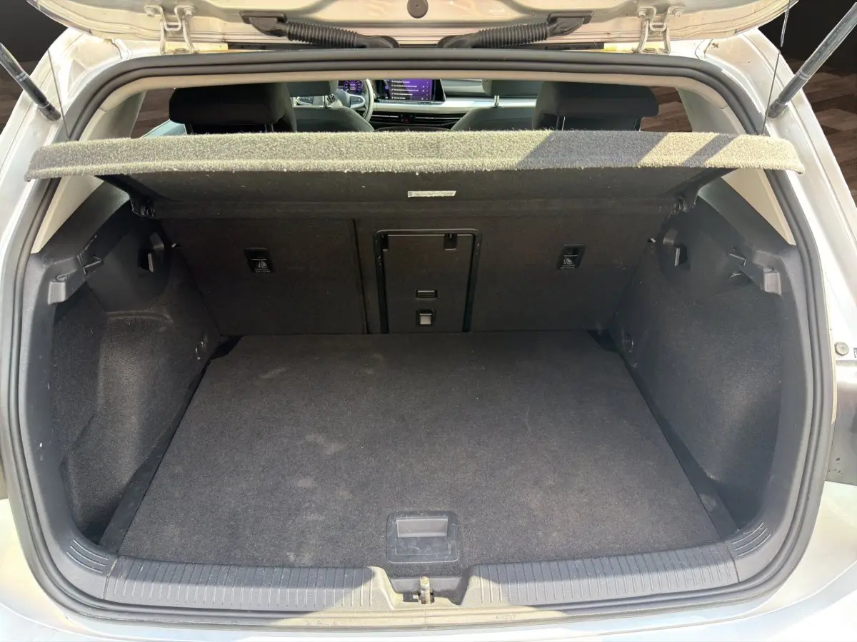 Vue arrière du coffre ouvert d'une Volkswagen Golf gris clair, montrant l'espace de chargement vide et la tablette de coffre relevée.