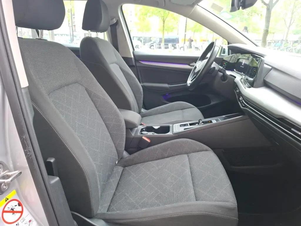 Intérieur de la Volkswagen Golf 1.0 ETSI gris clair, vue côté conducteur, sièges tissu et tableau de bord moderne avec écran tactile.
