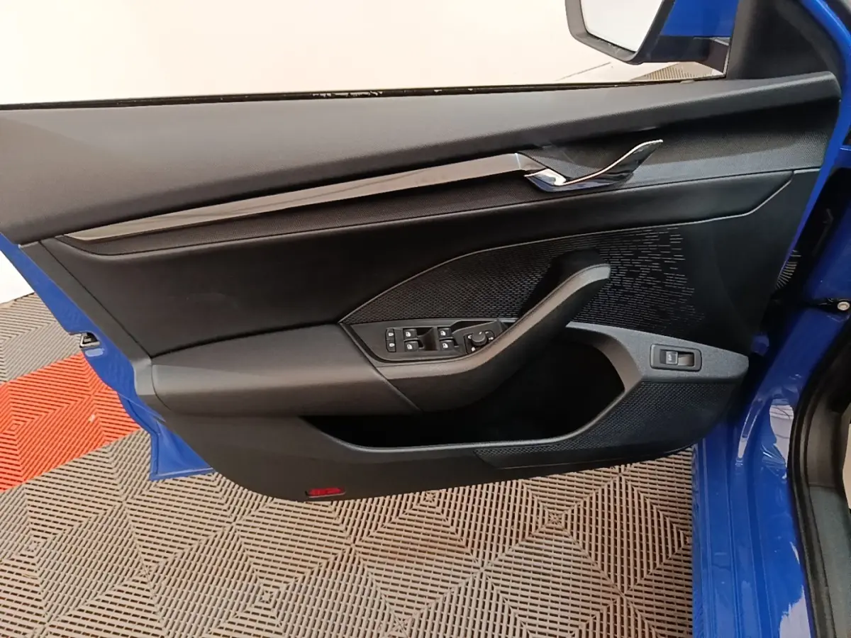 Vue intérieure côté gauche de la porte avant bleue d'une Skoda Octavia 2024 avec commandes électriques et garniture noire.