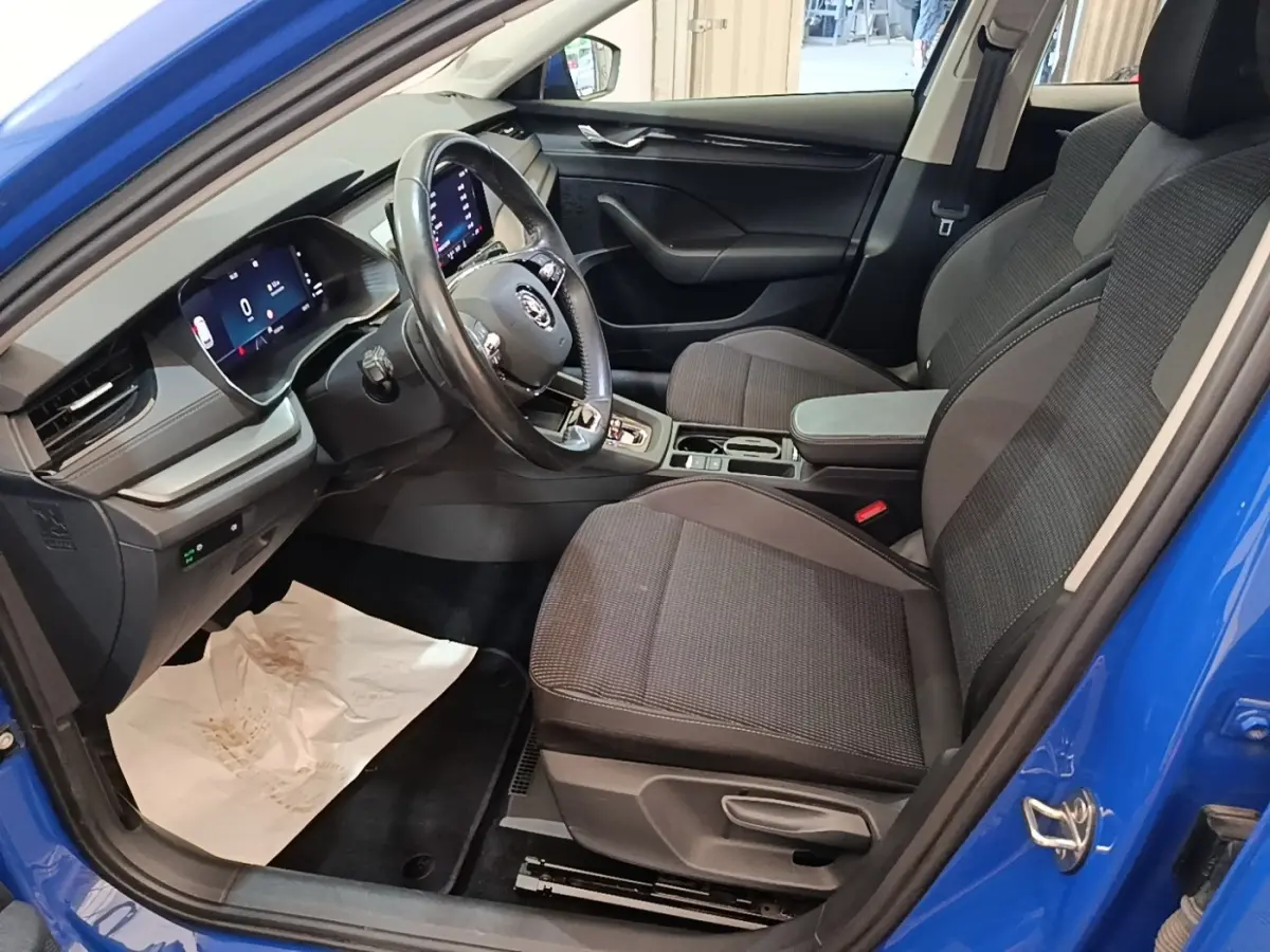 Vue intérieure côté conducteur de la Skoda Octavia 2024 bleue, avec sièges tissu gris et tableau de bord numérique.