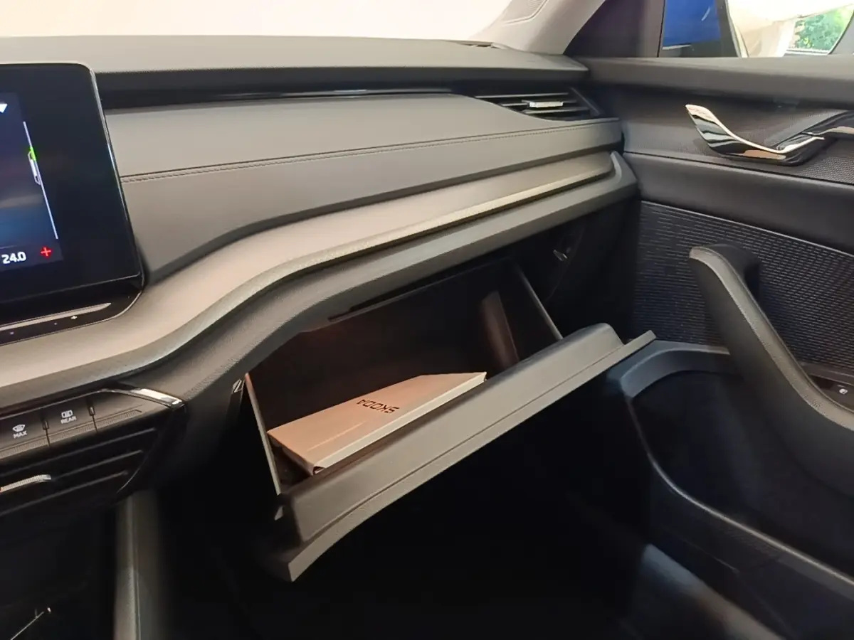 Intérieur de la Skoda Octavia 2024, vue côté passager sur la boîte à gants ouverte avec manuel visible, finition noire.