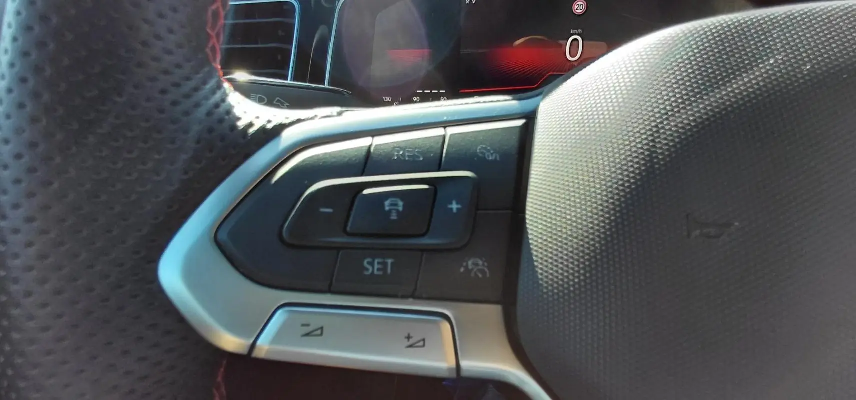 Gros plan sur les commandes du volant sport de la Volkswagen Polo GTI 2024, avec finition noire et surpiqûres rouges.