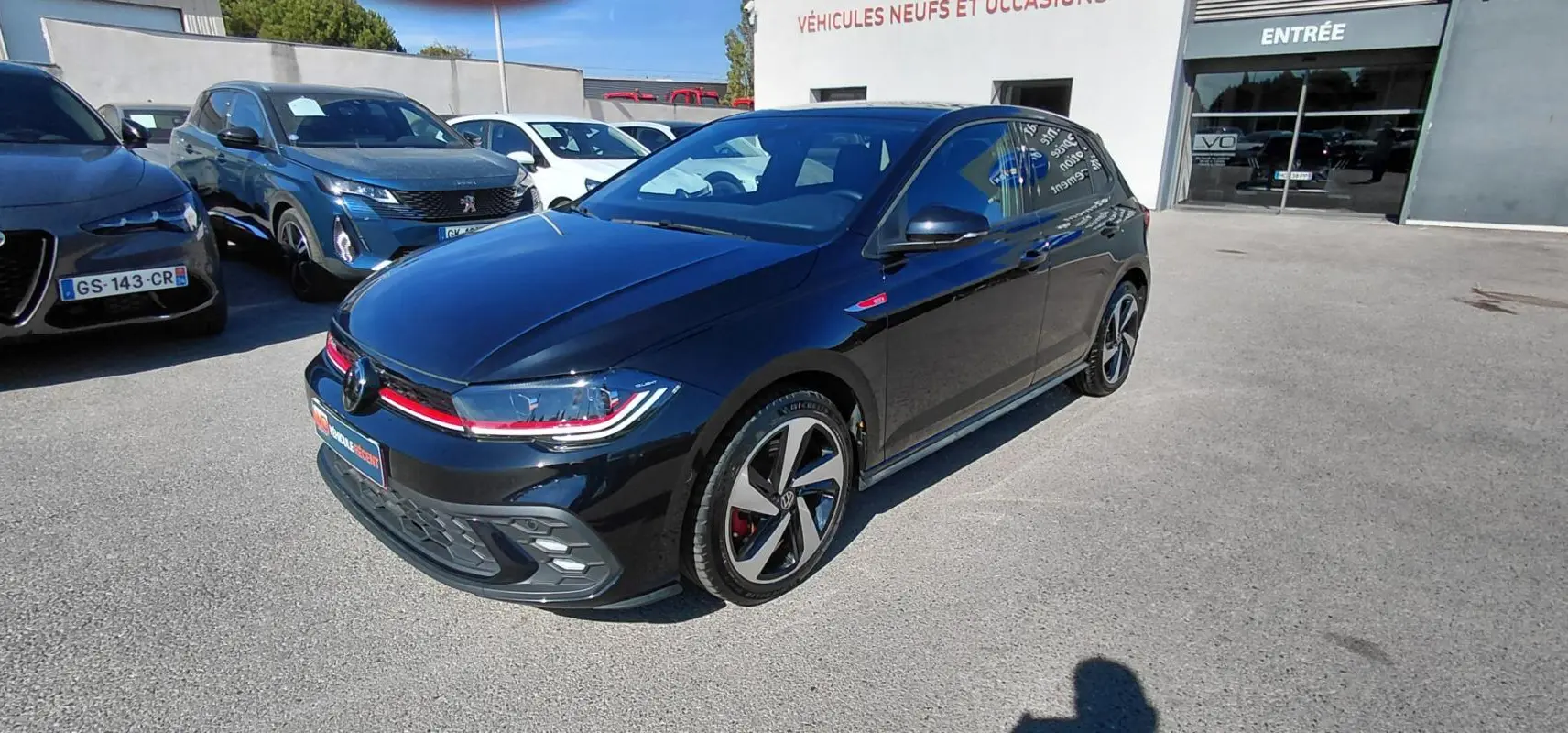 Volkswagen Polo GTI noir vue 3/4 avant droit, jantes alliage 17 pouces et bande rouge distinctive sur calandre.