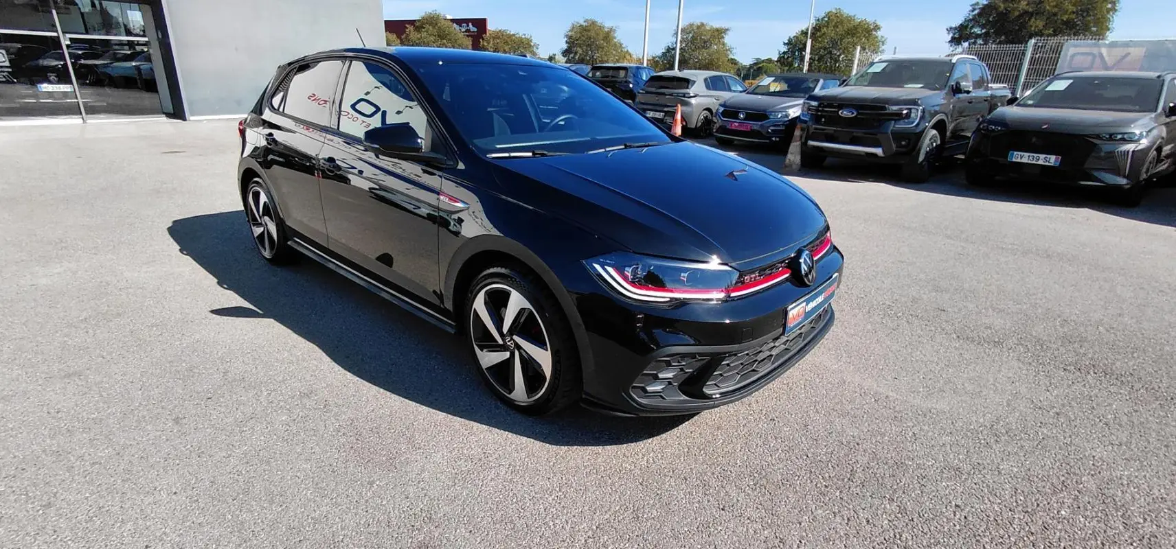 Volkswagen Polo GTI noire vue 3/4 avant droit avec jantes alliage 17 pouces et bande rouge distinctive.