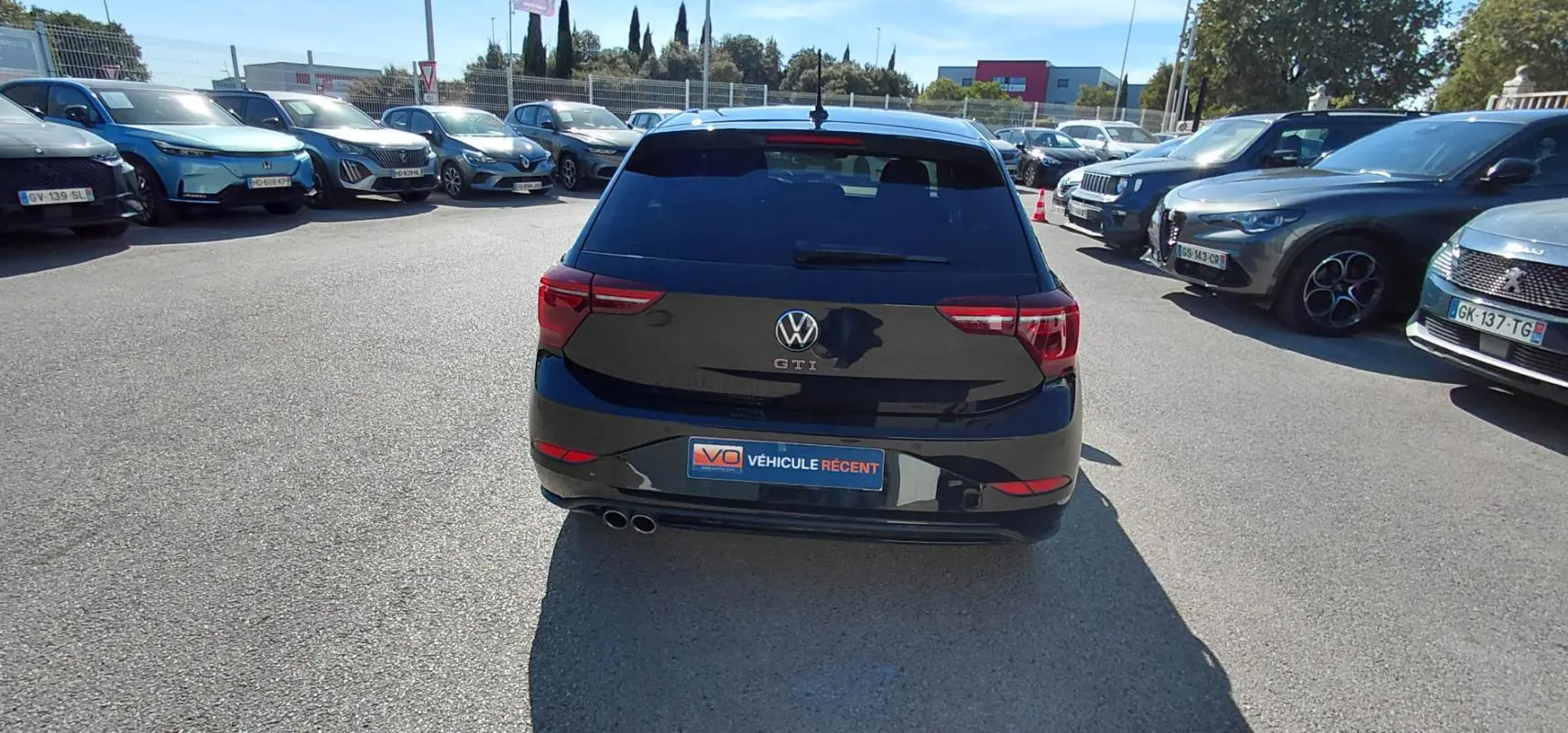 Vue arrière d'une Volkswagen Polo GTI noire 2024 avec double sortie d'échappement et vitres teintées, stationnée en extérieur.