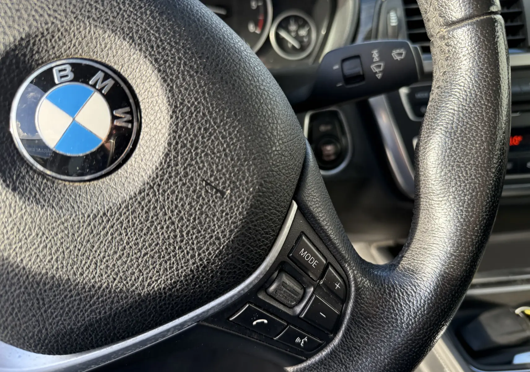 Gros plan sur le volant en cuir noir avec logo BMW au centre et commandes multimédia sur le côté droit, intérieur d'une Série 3 gris.