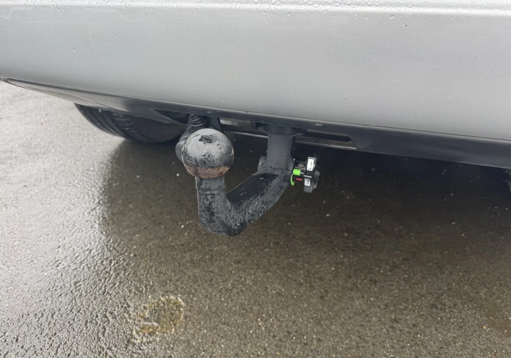 Gros plan sur l'attelage d'une Jeep Compass gris 2023, visible sous le pare-chocs arrière sur sol humide.