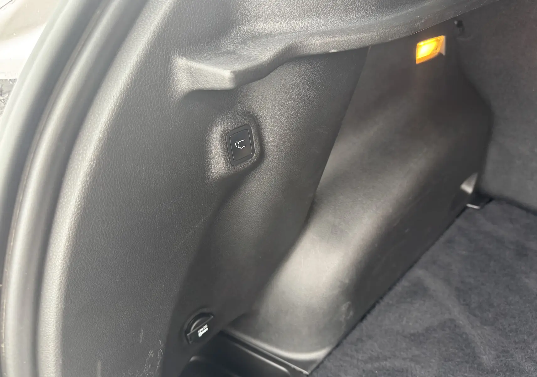 Détail de l'intérieur du coffre côté gauche du Jeep Compass gris 2023, avec bouton de rabattement des sièges et lumière orange allumée.