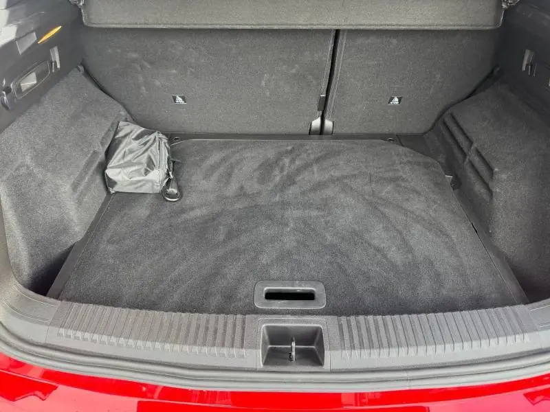 Coffre ouvert vu de l'arrière d'un Renault Austral rouge, avec tapis de sol noir et rangement latéral.