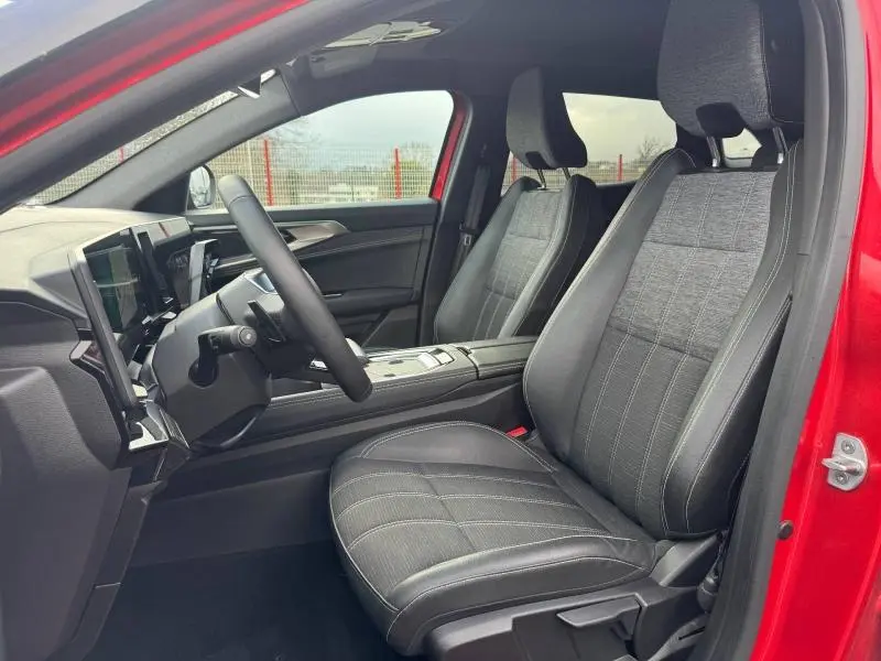 Vue intérieure côté conducteur du Renault Austral rouge, sièges en tissu gris clair avec surpiqûres blanches et tableau de bord moderne.