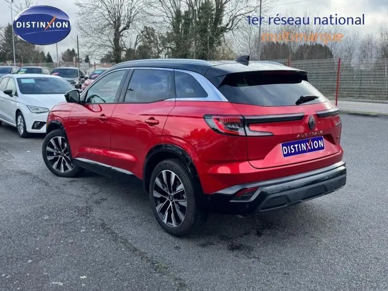 Vue 3/4 arrière droite du Renault Austral rouge flamme avec toit noir et jantes alliage sur parking extérieur.
