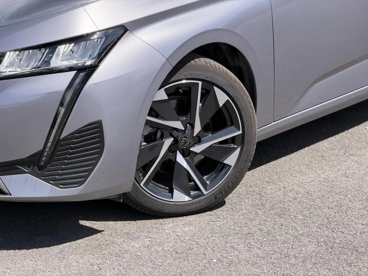 Gros plan sur la roue avant droite et le pare-chocs avant gris Artense d'une Peugeot 308 Hybrid 2025.