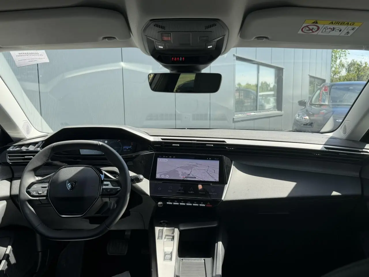 Vue intérieure avant du Peugeot 308 Hybrid 2025, tableau de bord noir avec écran tactile central affichant la navigation.