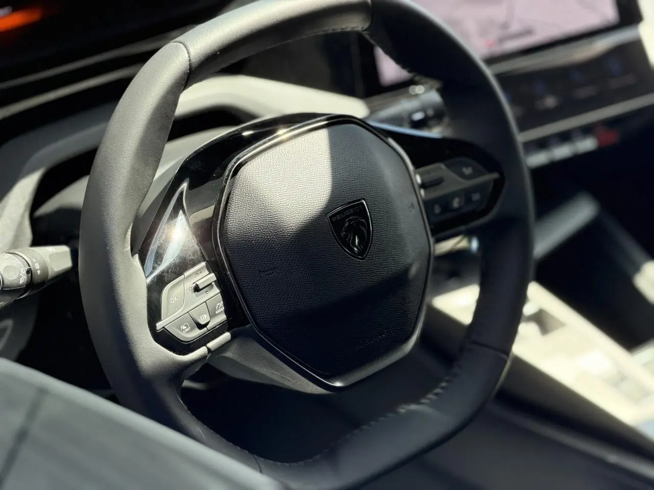 Gros plan sur le volant en cuir noir du Peugeot 308 Hybrid 145, avec commandes intégrées et logo central.