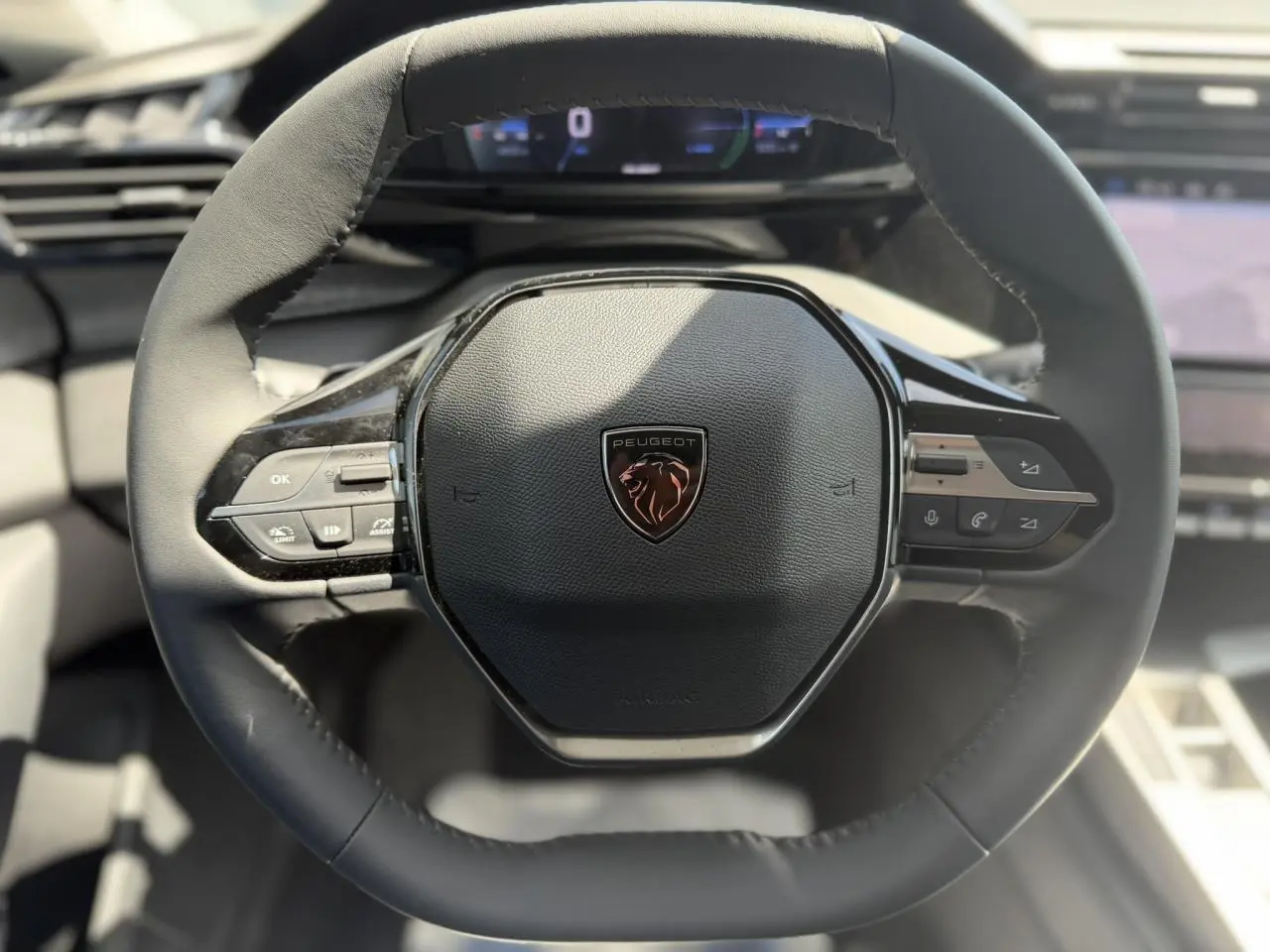 Vue rapprochée du volant cuir noir de la Peugeot 308 Hybrid 145 avec commandes intégrées et logo lion central.