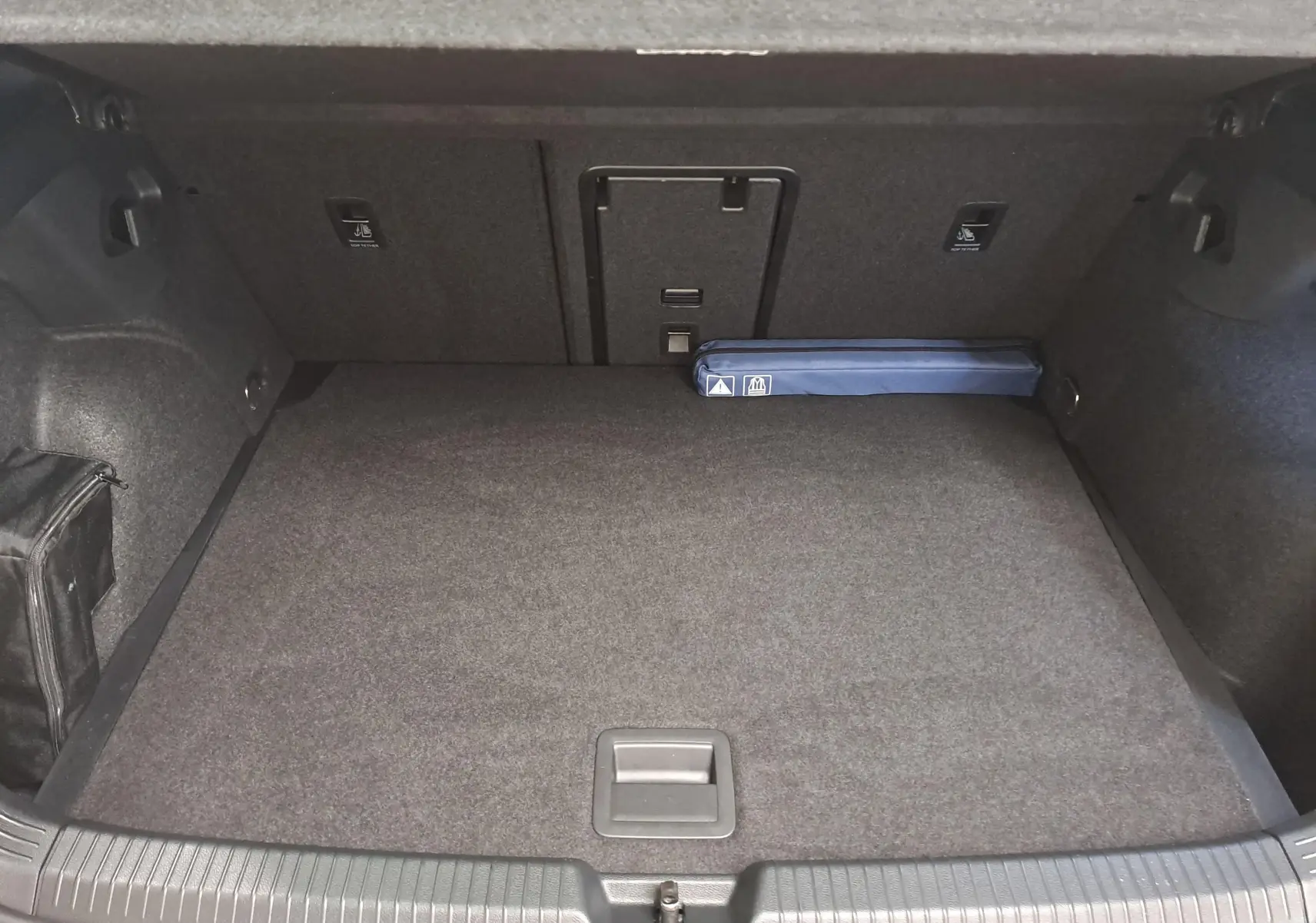 Coffre ouvert d’une Volkswagen Golf 2.0 TDI 150 DSG7 R Line noir grenadille, montrant un espace de chargement propre avec un kit de sécurité bleu.