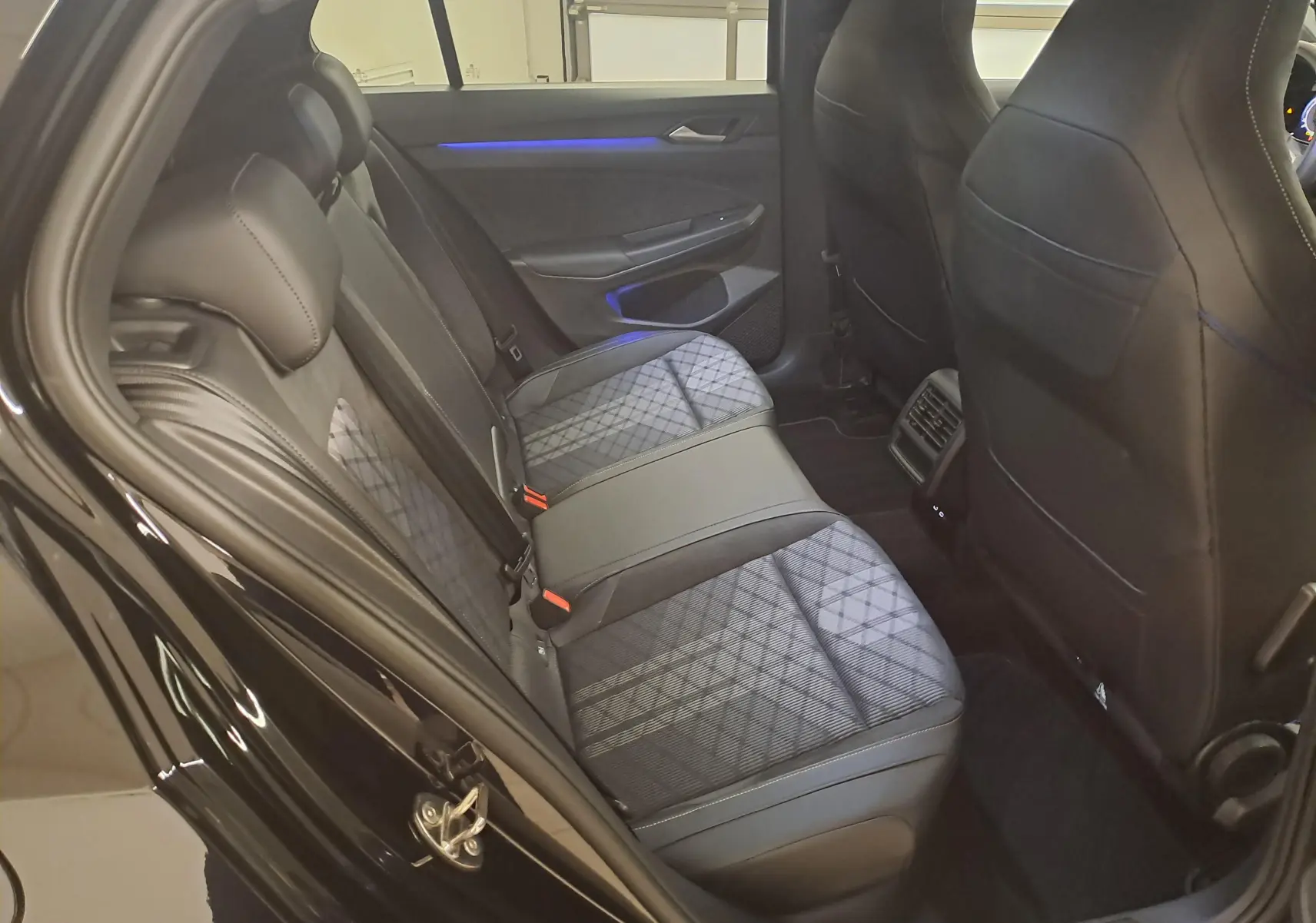 Vue intérieure arrière côté gauche de la Volkswagen Golf 2.0 TDI 150 DSG7 R Line 2024 avec sièges tissu et cuir noirs à motif géométrique.