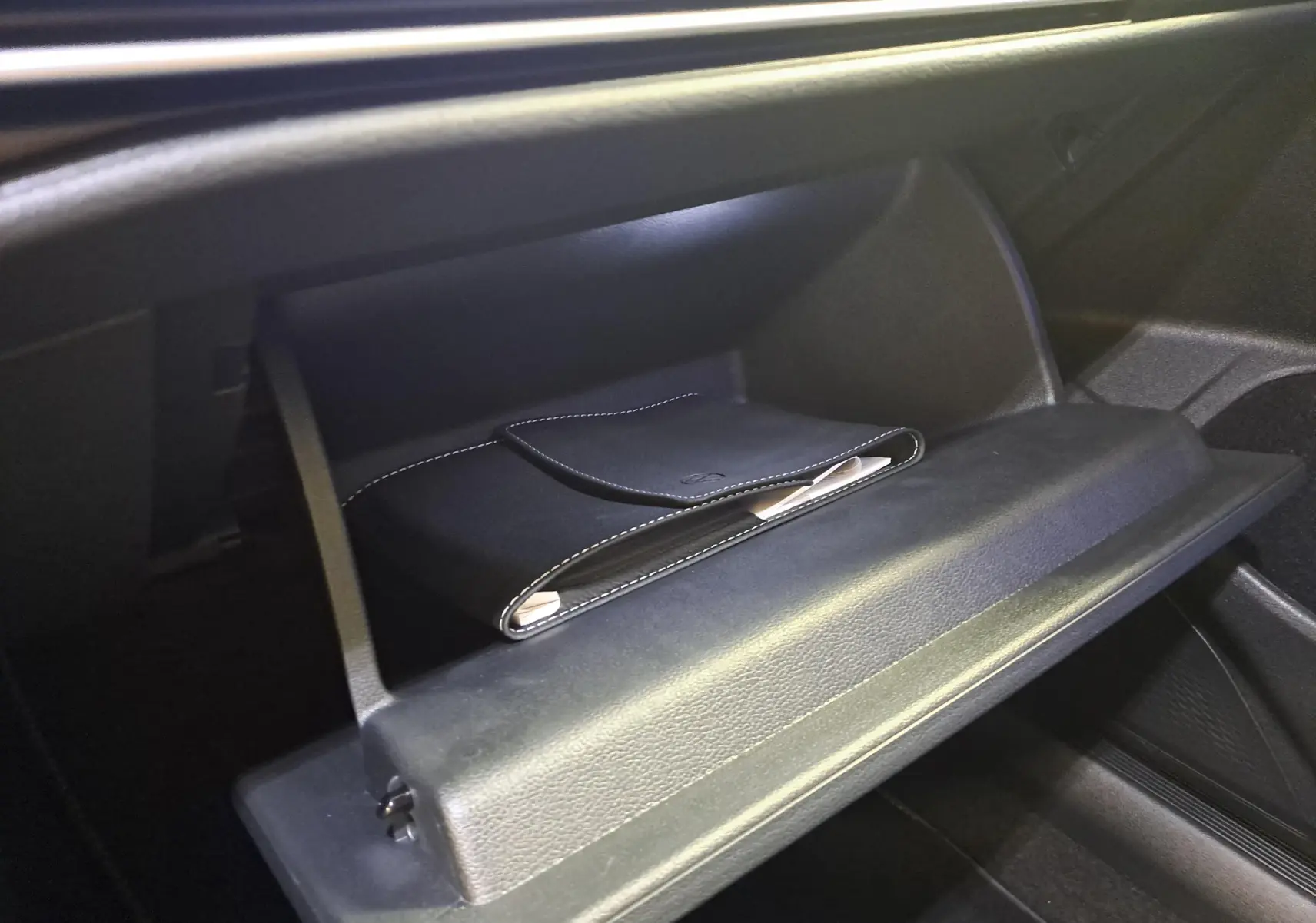 Vue rapprochée de la boîte à gants ouverte de la Volkswagen Golf 2.0 TDI 150 DSG7 R Line noire grenadille, avec pochette en cuir noir.