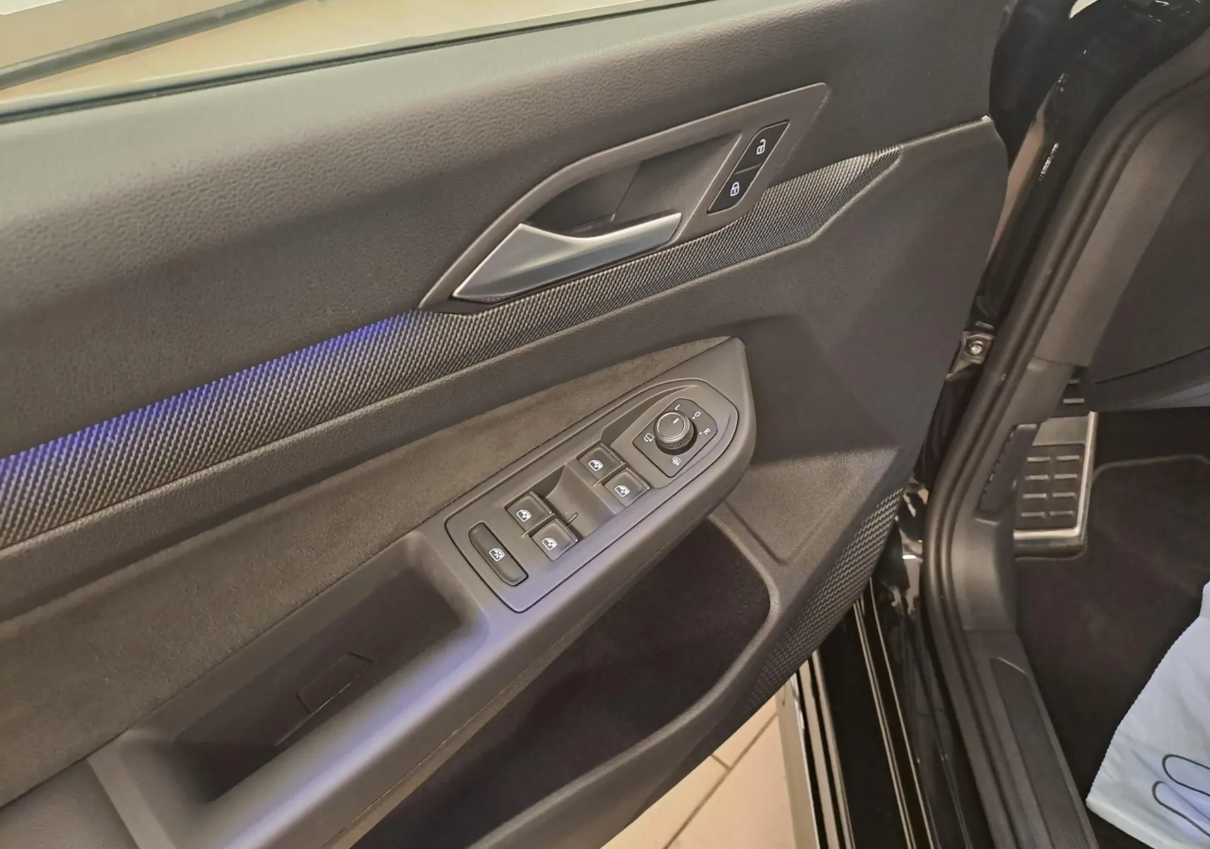 Vue rapprochée de la porte avant gauche noire grenadille d’une Volkswagen Golf 2.0 TDI 150 DSG7 R Line avec commandes de vitres et rétroviseurs.
