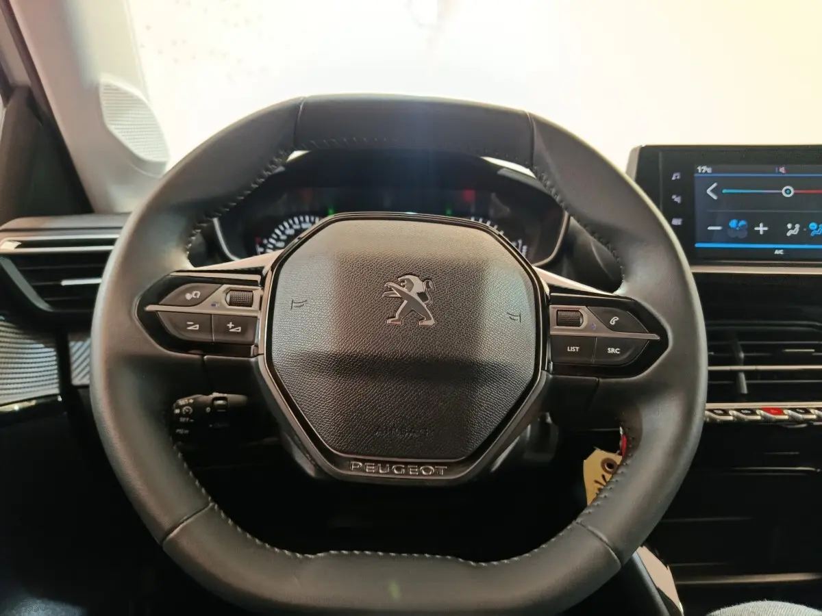 Vue rapprochée du volant cuir multifonctions noir d'une Peugeot 208 2023 avec tableau de bord et écran tactile visible à droite.