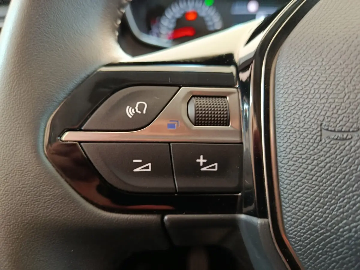 Gros plan sur les commandes multifonctions noires du volant cuir du Peugeot 208 blanc, version 2023 PureTech 75 S&S Style.