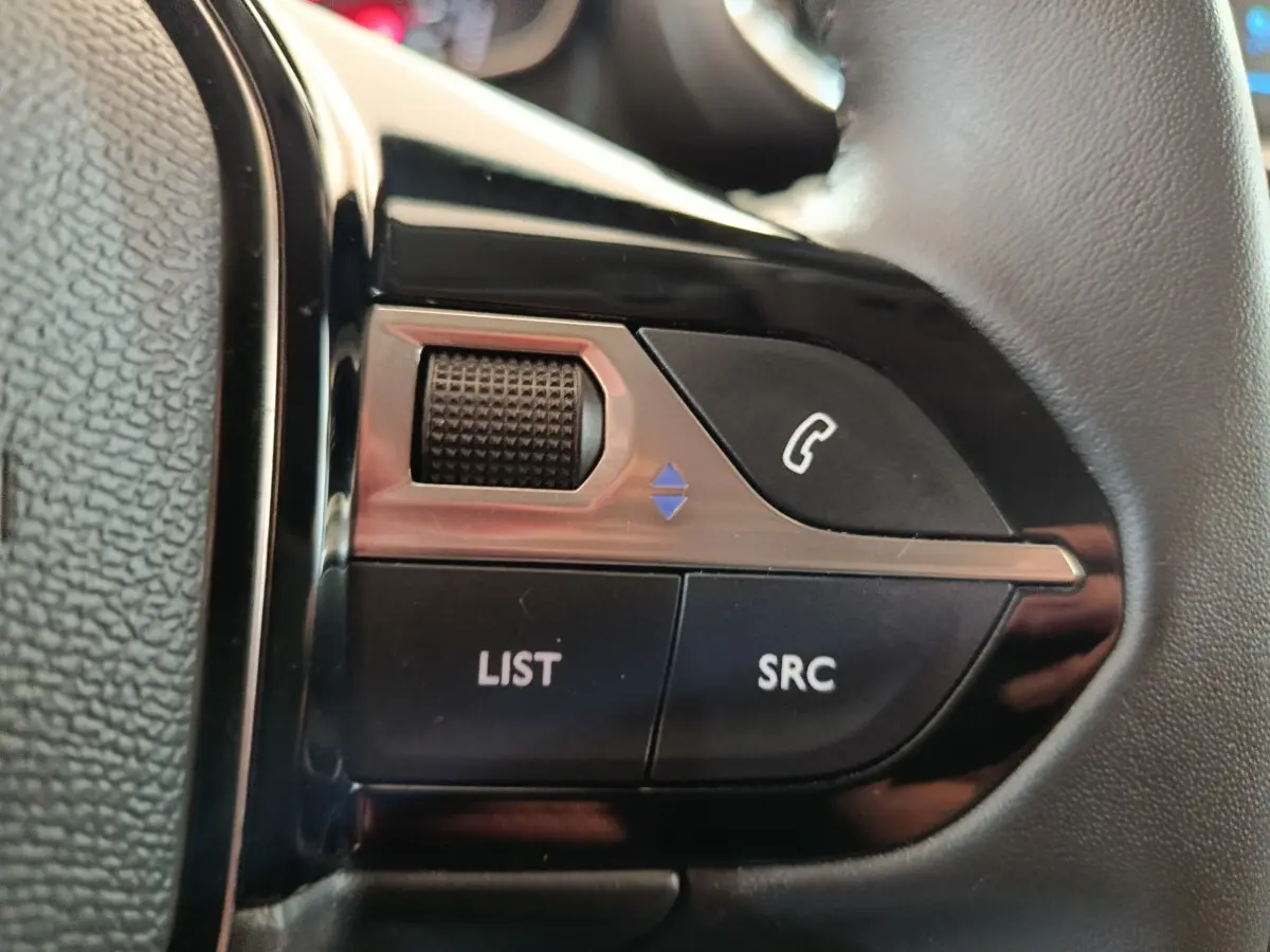 Gros plan sur les commandes multifonctions en cuir du volant côté gauche d'une Peugeot 208 blanche 2023.