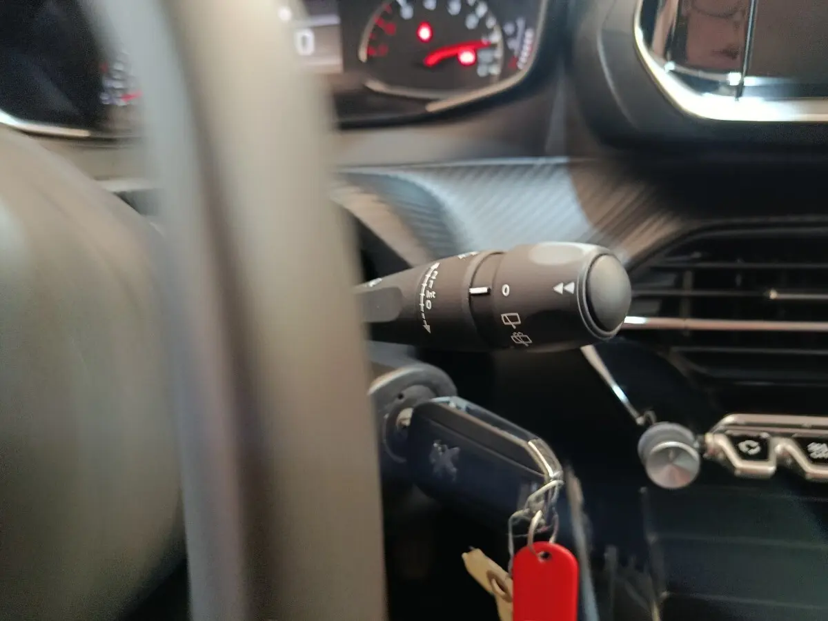 Détail intérieur du tableau de bord de la Peugeot 208 blanc, avec clé insérée et commandes au volant visibles.