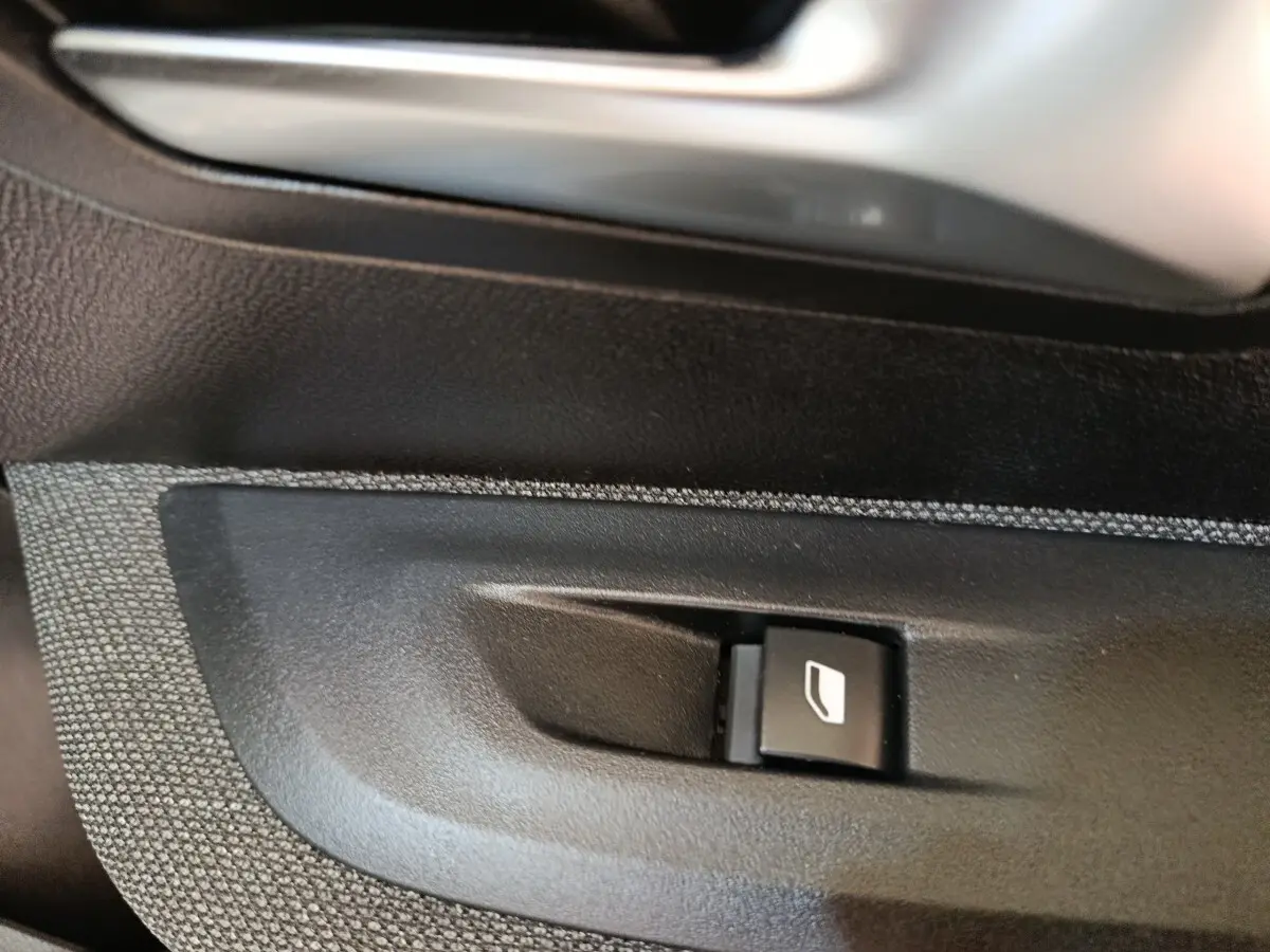 Gros plan sur le bouton de commande de la vitre électrique côté conducteur d'une Peugeot 208 blanche 2023.