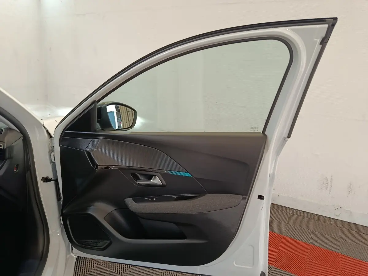 Vue intérieure de la porte avant gauche blanche d'une Peugeot 208 2023 avec garniture noire et détails texturés.