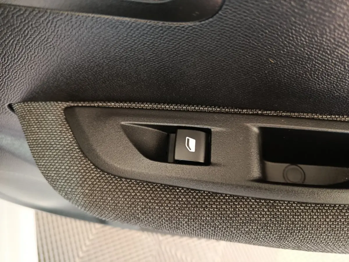 Gros plan sur le bouton de commande de lève-vitre intégré dans la garniture noire texturée d’une Peugeot 208 blanche.