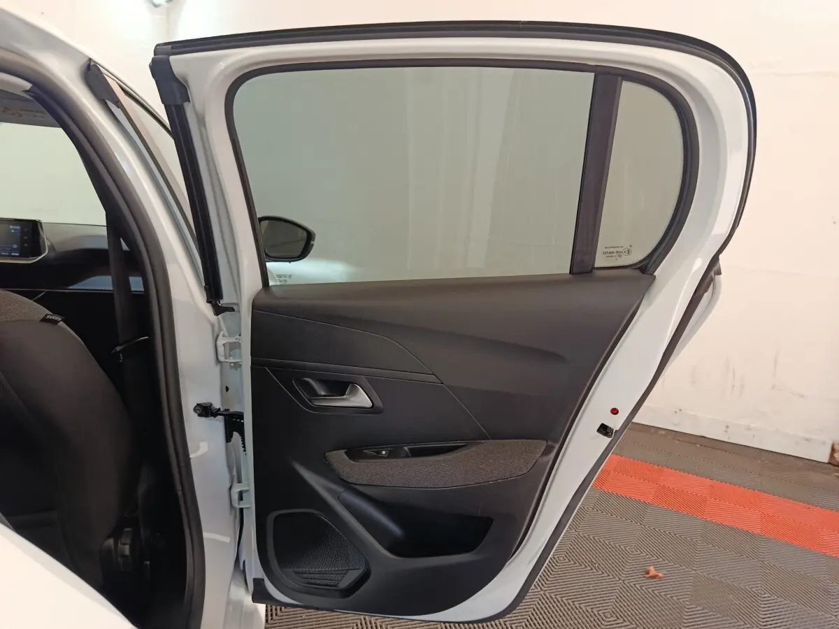 Vue de profil de la porte arrière droite blanche d'une Peugeot 208 2023 avec garniture intérieure noire et tissu gris.