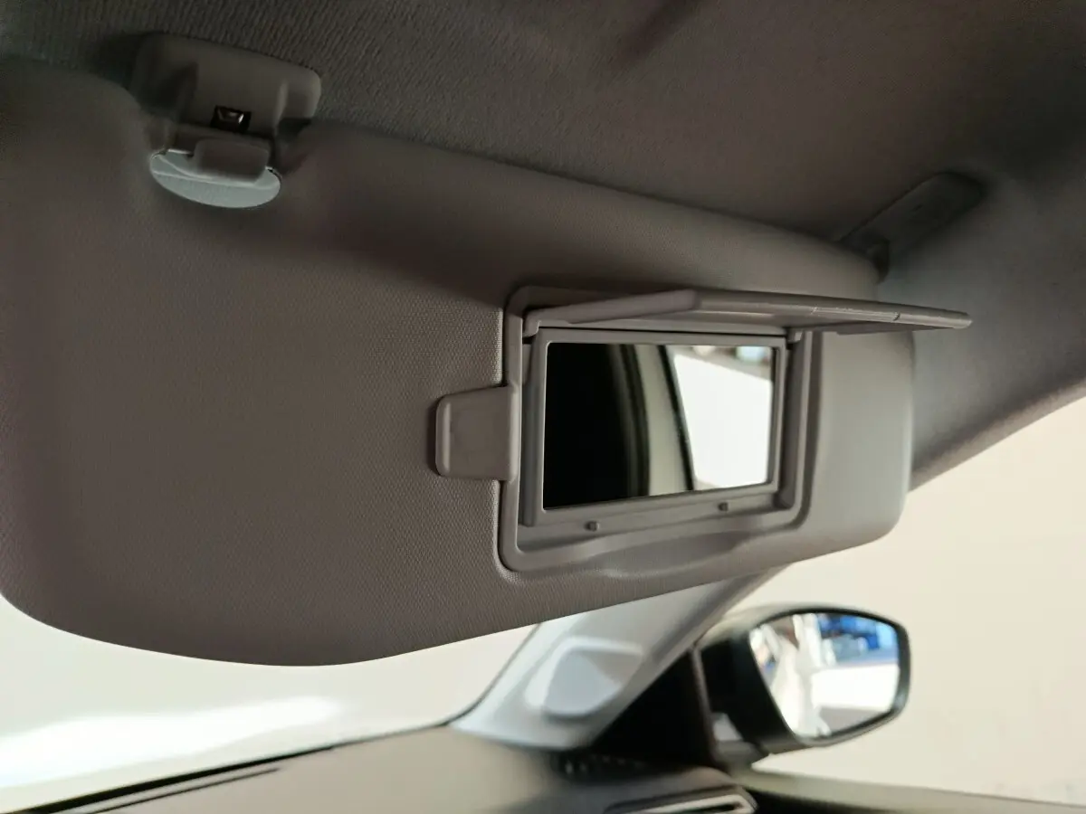 Miroir de courtoisie ouvert sur pare-soleil gris clair côté conducteur dans l’habitacle d’une Peugeot 208 blanche.