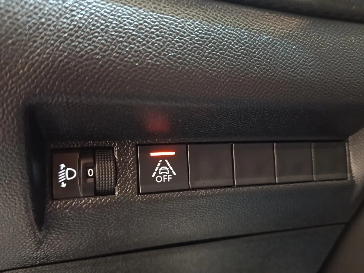Gros plan sur les commandes de réglage des phares et désactivation de l’aide au maintien de voie dans une Peugeot 208 blanche.