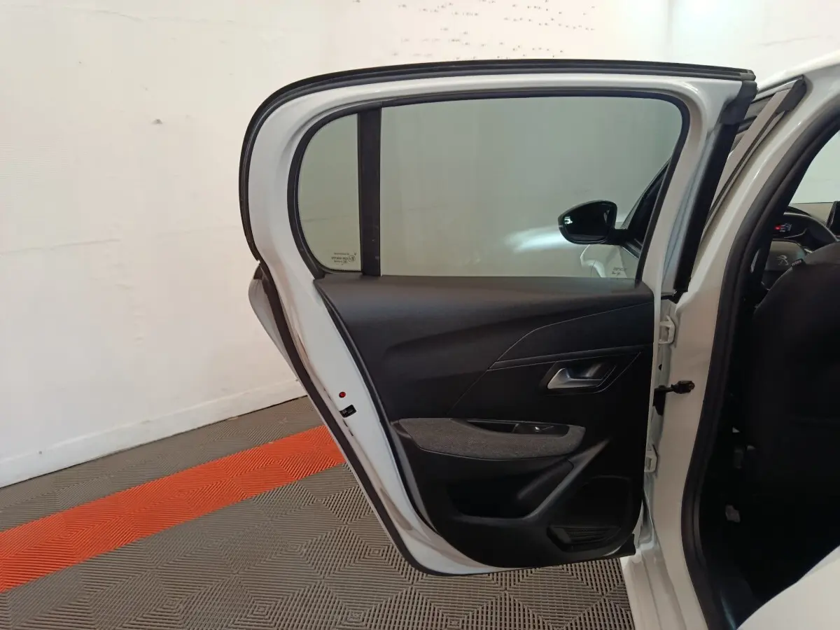 Vue intérieure de la porte arrière droite ouverte d'une Peugeot 208 blanche, avec garniture noire et fenêtre teintée.