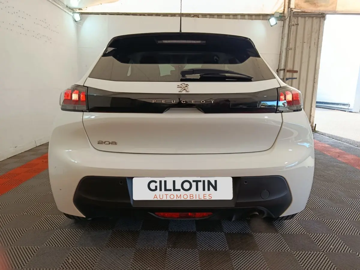 Vue arrière d'une Peugeot 208 blanche 2023 avec feux LED et bande noire distinctive sur le hayon.