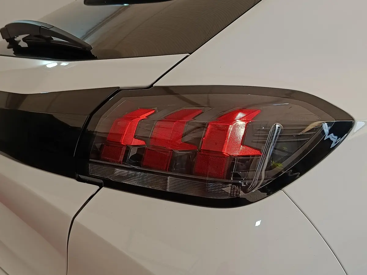 Gros plan sur le feu arrière droit rouge d'une Peugeot 208 blanche, soulignant le design moderne du véhicule.