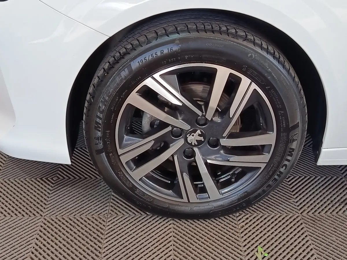 Gros plan sur la roue avant droite d'une Peugeot 208 blanche, avec jante alliage bicolore et pneu Michelin.