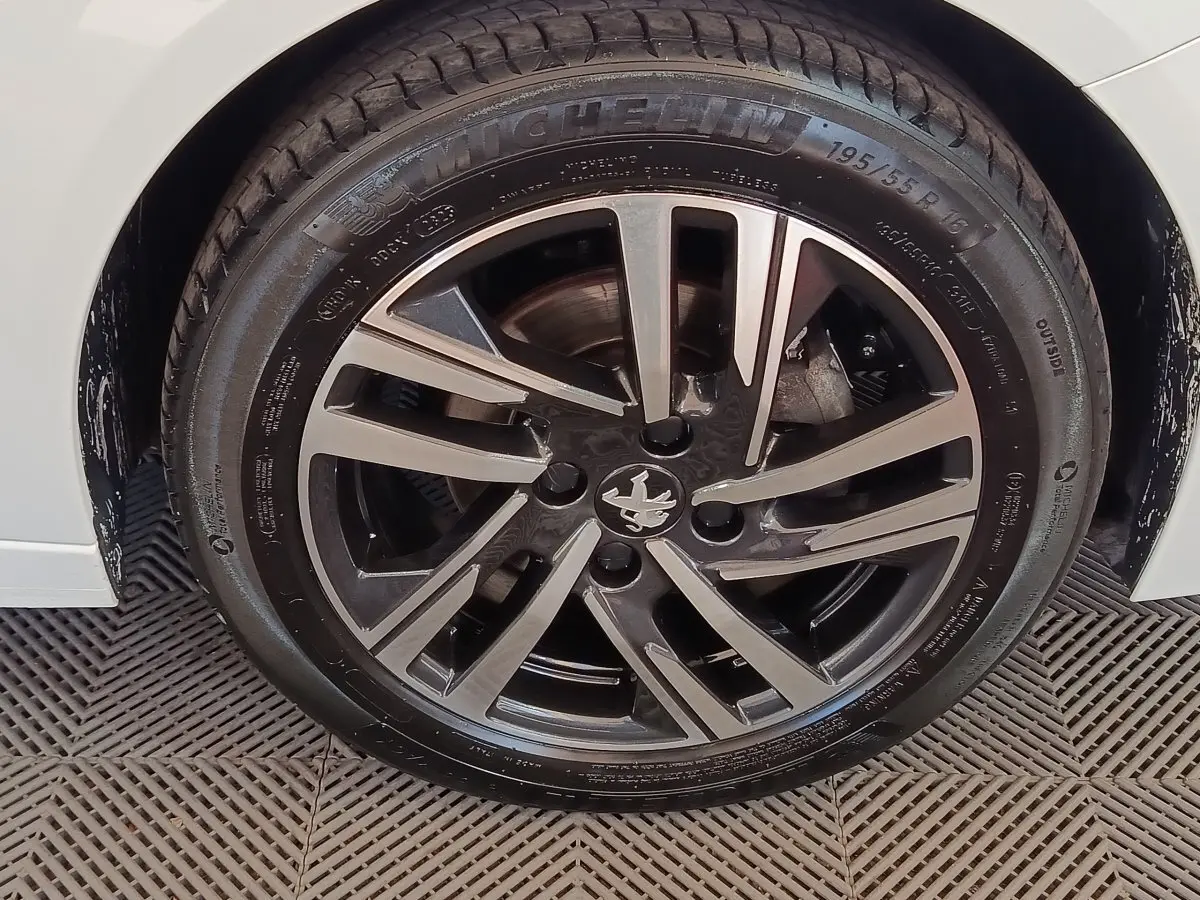 Gros plan sur la roue avant droite d'une Peugeot 208 blanche, jante alliage noire et argent avec logo lion central.