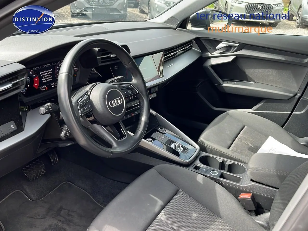Intérieur avant de l'Audi A3 Sportback 2023 en gris, vue côté conducteur montrant le volant multifonction et la console centrale.