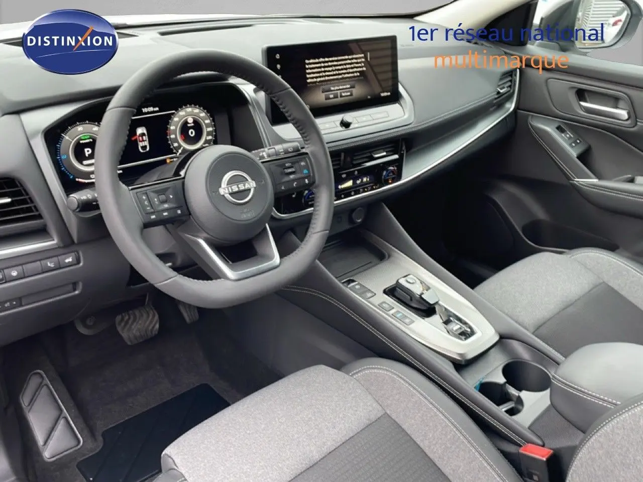 Vue intérieure du poste de conduite du Nissan Qashqai 2025, avec volant multifonction, écran tactile et sellerie tissu gris.