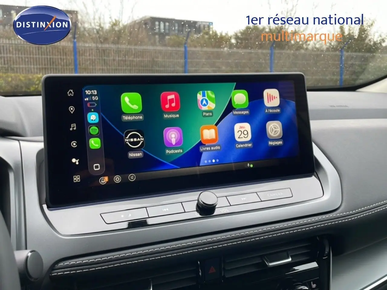 Écran tactile central du Nissan Qashqai 2025 affichant l’interface Apple CarPlay, avec tableau de bord gris et coutures blanches.