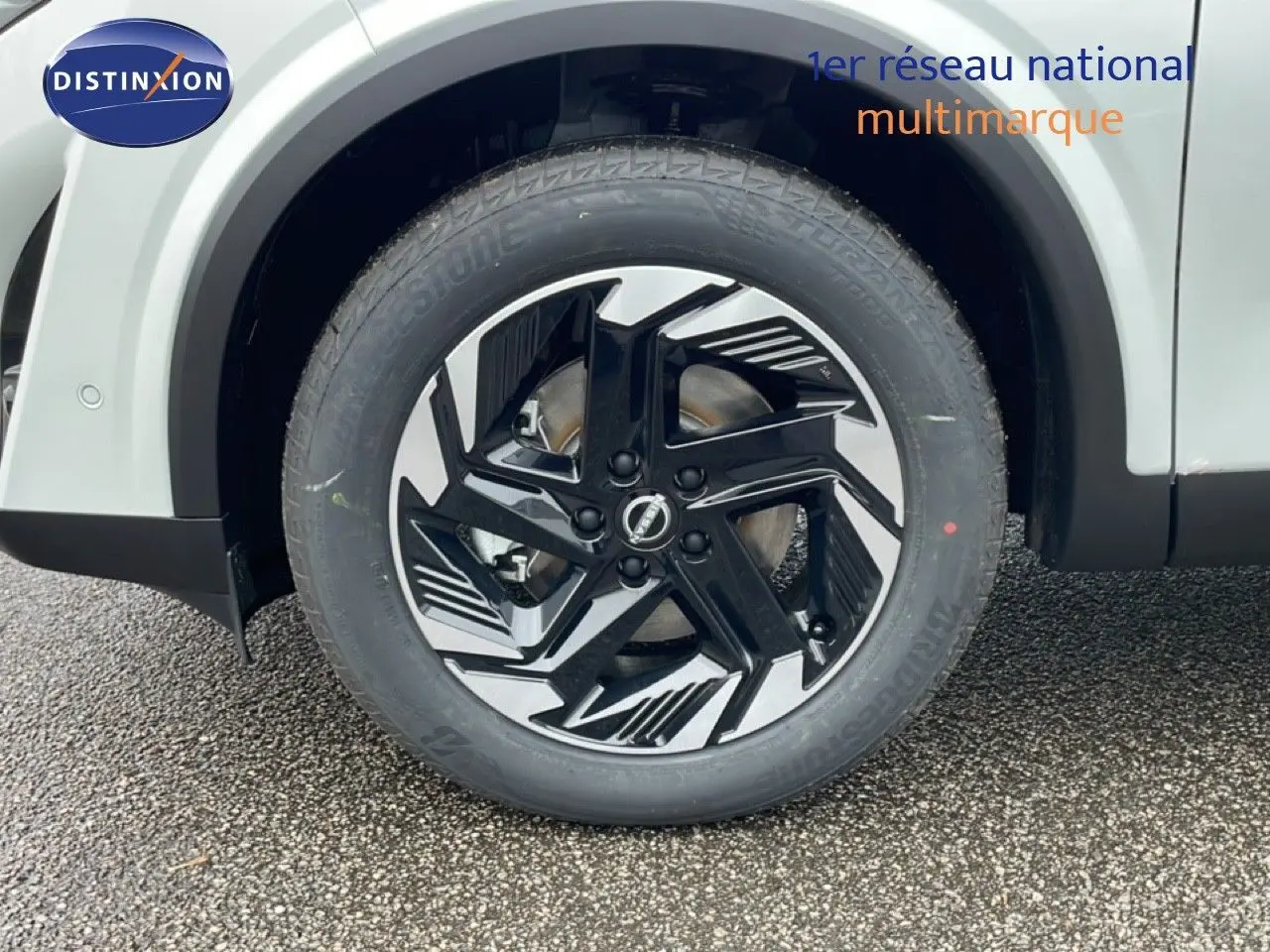 Gros plan sur la roue avant gauche du Nissan Qashqai blanc nacré, avec jante alliage noire et argentée au design moderne.